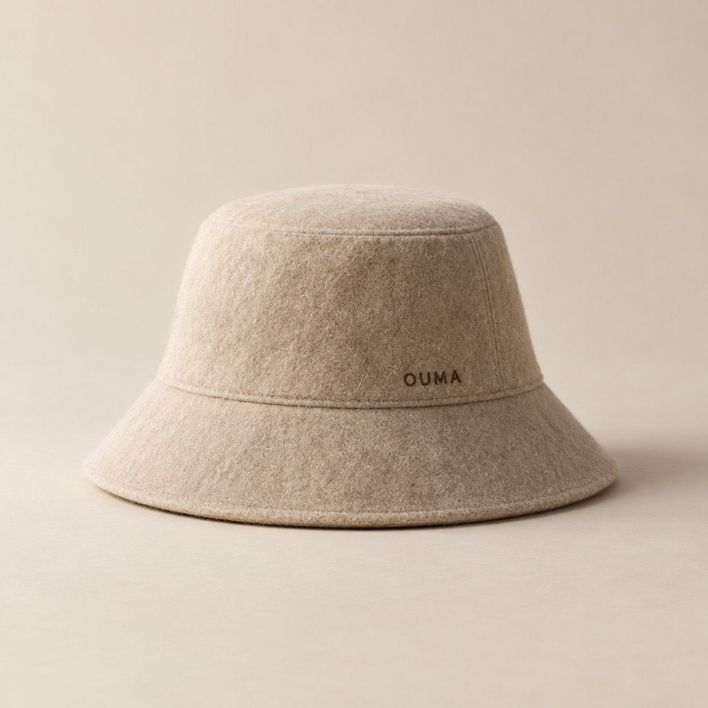 Beige bucket-style OUMA sauna hat with discreet branding — AI-generated concept.